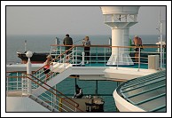 Passengers watch as cargo ship passes Empress of the Seas heading back into the bay.